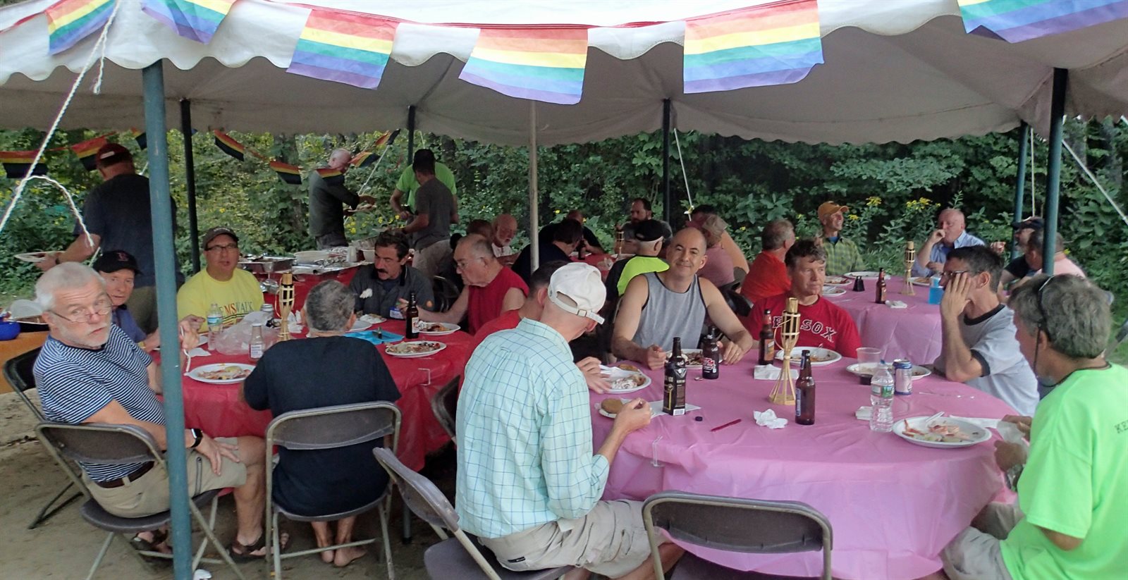 GayOutdoors members sharing a meal under a rainbow-flag tent at the Saturday potluck