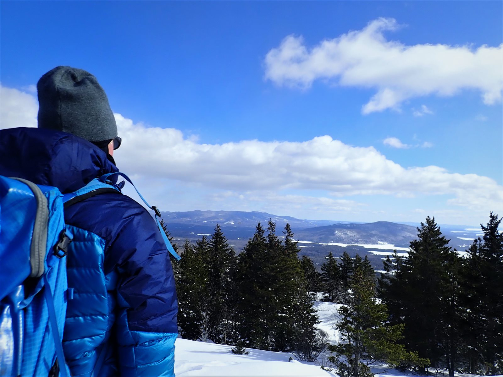 A hiker seen from behind in a warm hat and jacket overlooking a snowy winter landscape
